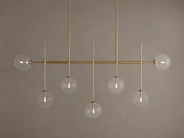 Roscoe Linear Chandelier: 7 illuminated clear glass globe lights on a brass-finished horizontal bar. Angled view.