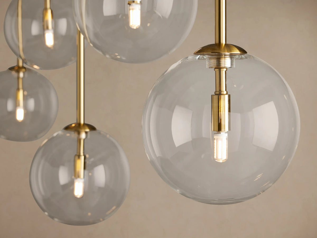 Roscoe Linear Chandelier, brass-finished, with 7 clear glass globes on a horizontal bar and hanging vertically, beige background.