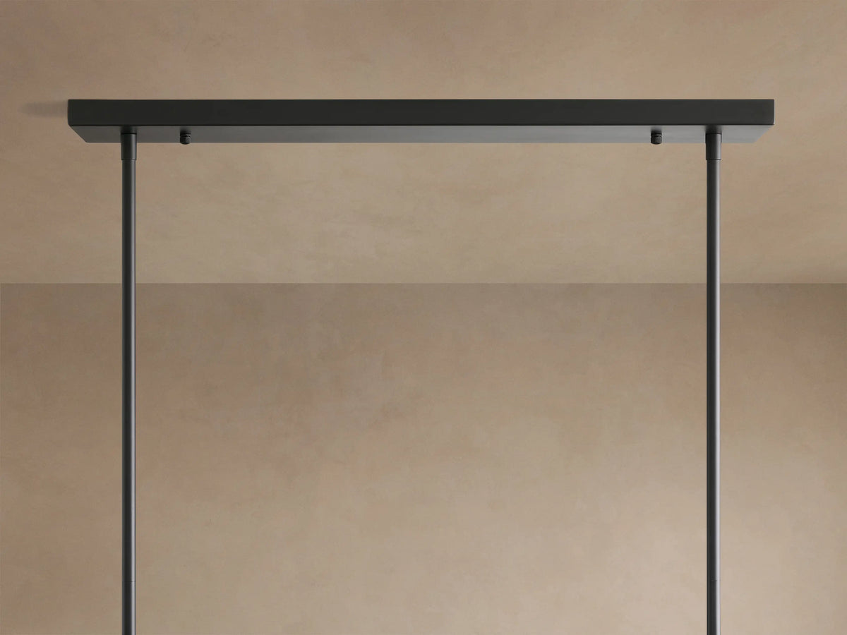 Close-up of Roscoe Linear Chandelier: clear glass globes with glowing LED bulbs, dark metal rods, soft beige background.