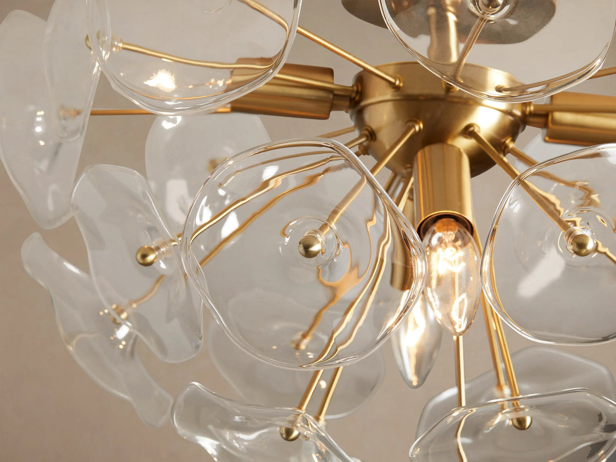 Lily Flush Mount ceiling light with a brass base and clear glass petals, angled view against a beige ceiling.