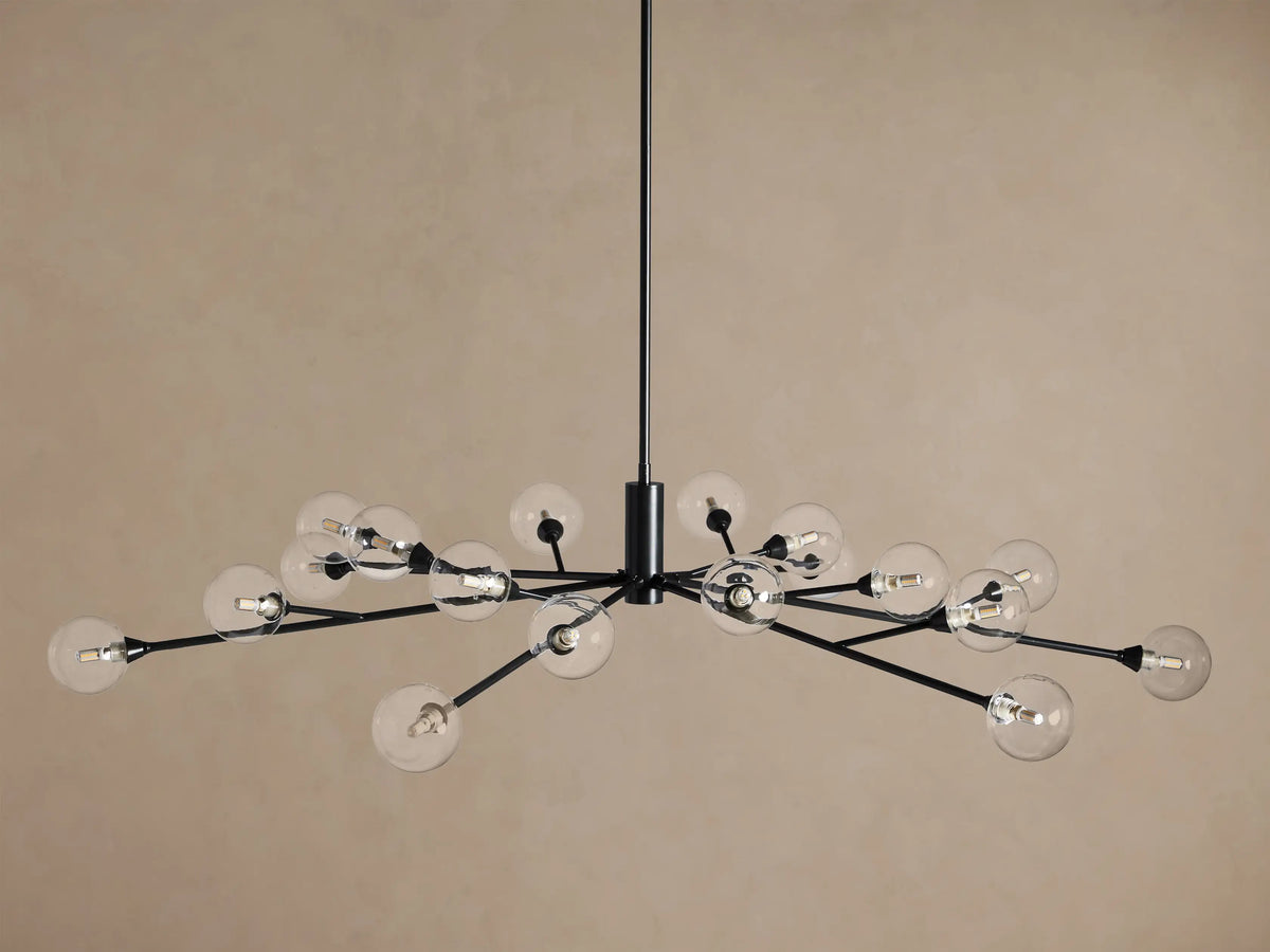 Apollo Round Chandelier, black metal stem and radiating arms with clear glass globes, each with a lit bulb, on a tan wall.