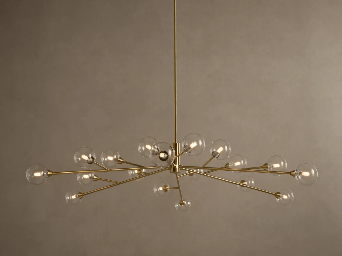 Apollo Round Chandelier: Brass-toned arms with many illuminated clear glass globe bulbs, suspended against a textured wall.