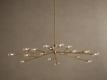 Apollo Round Chandelier: Brass-toned arms with many illuminated clear glass globe bulbs, suspended against a textured wall.