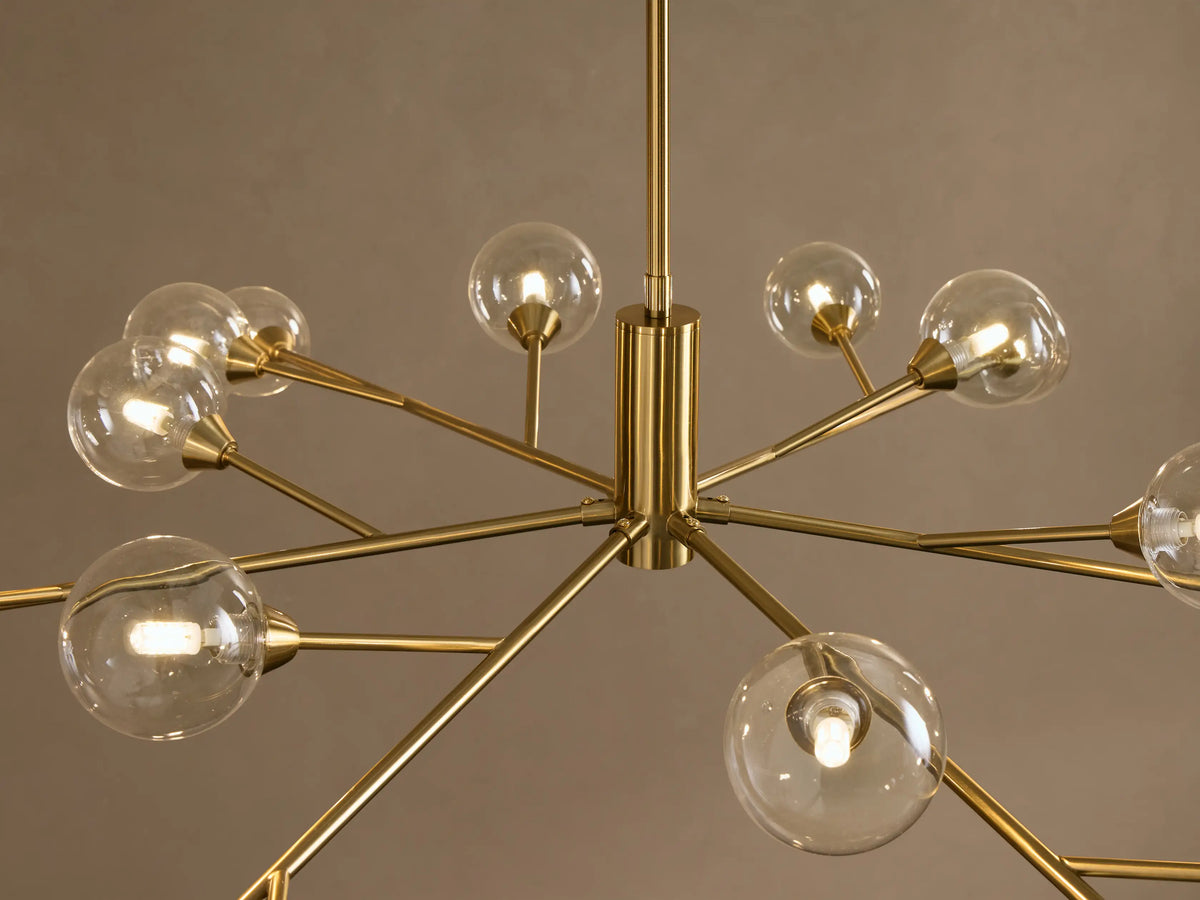 Apollo Round Chandelier: polished gold frame, starburst design, with many clear spherical bulbs against a neutral wall.