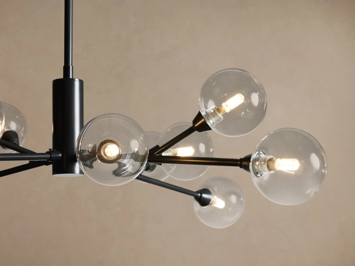 Apollo Round Chandelier, black metal frame with 12 radiating arms holding clear spherical bulbs, suspended against a light brown wall.