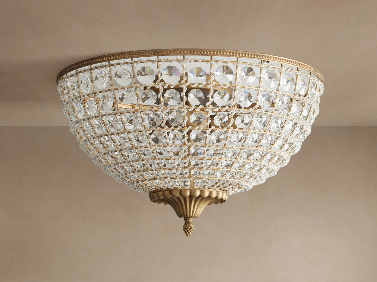 Poppy Flush Mount. Dome-shaped fixture with rows of clear faceted crystals and antique brass accents, glowing warmly on a ceiling.