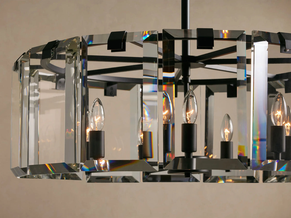 Amaya Round Chandelier, clear crystal panels in a dark frame, with lit candelabra bulbs and rainbow light reflections.