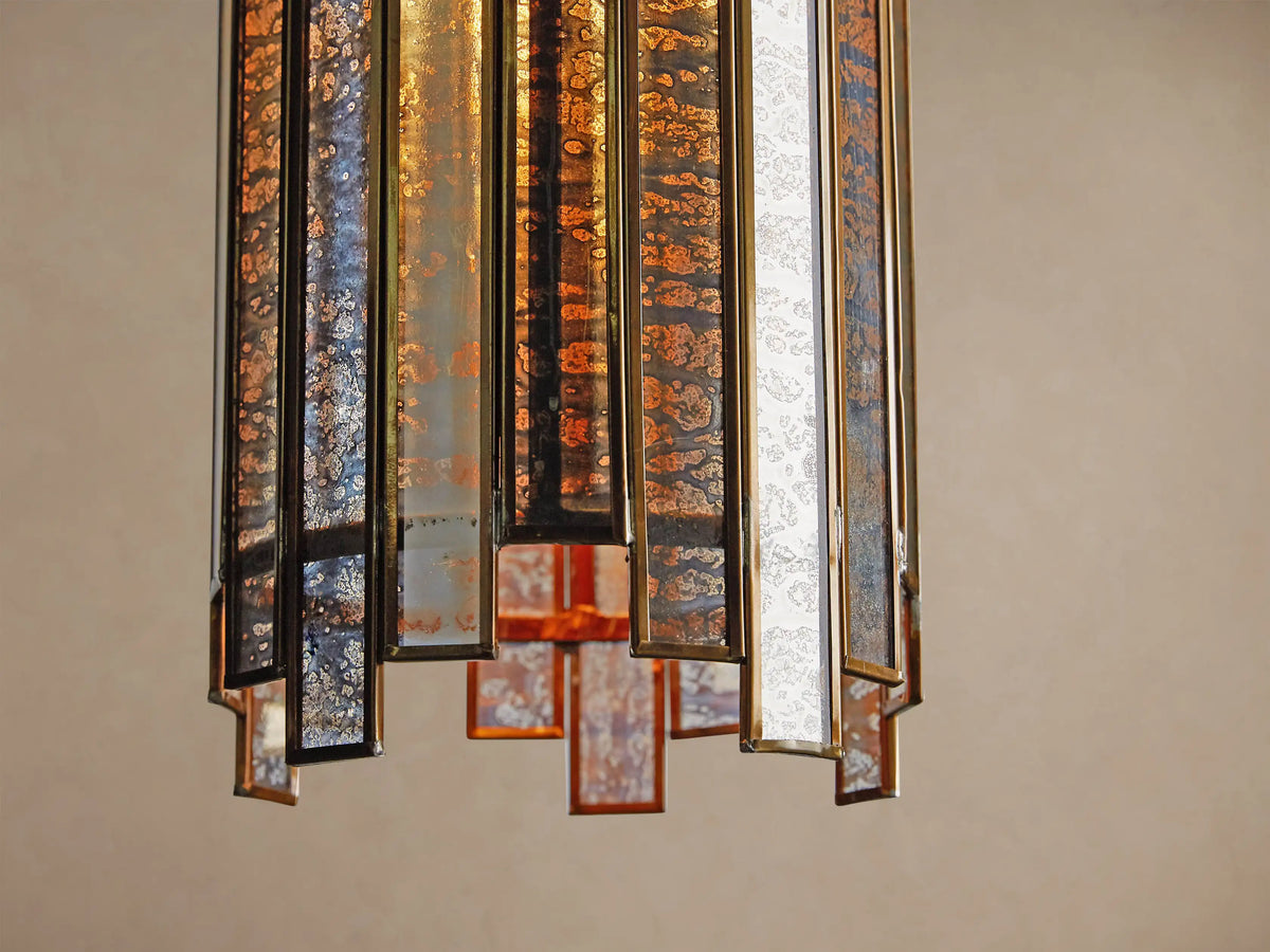 Laila Pendant, a cylindrical light with vertical antiqued mirrored-glass panels and an antique copper frame, glowing warmly.