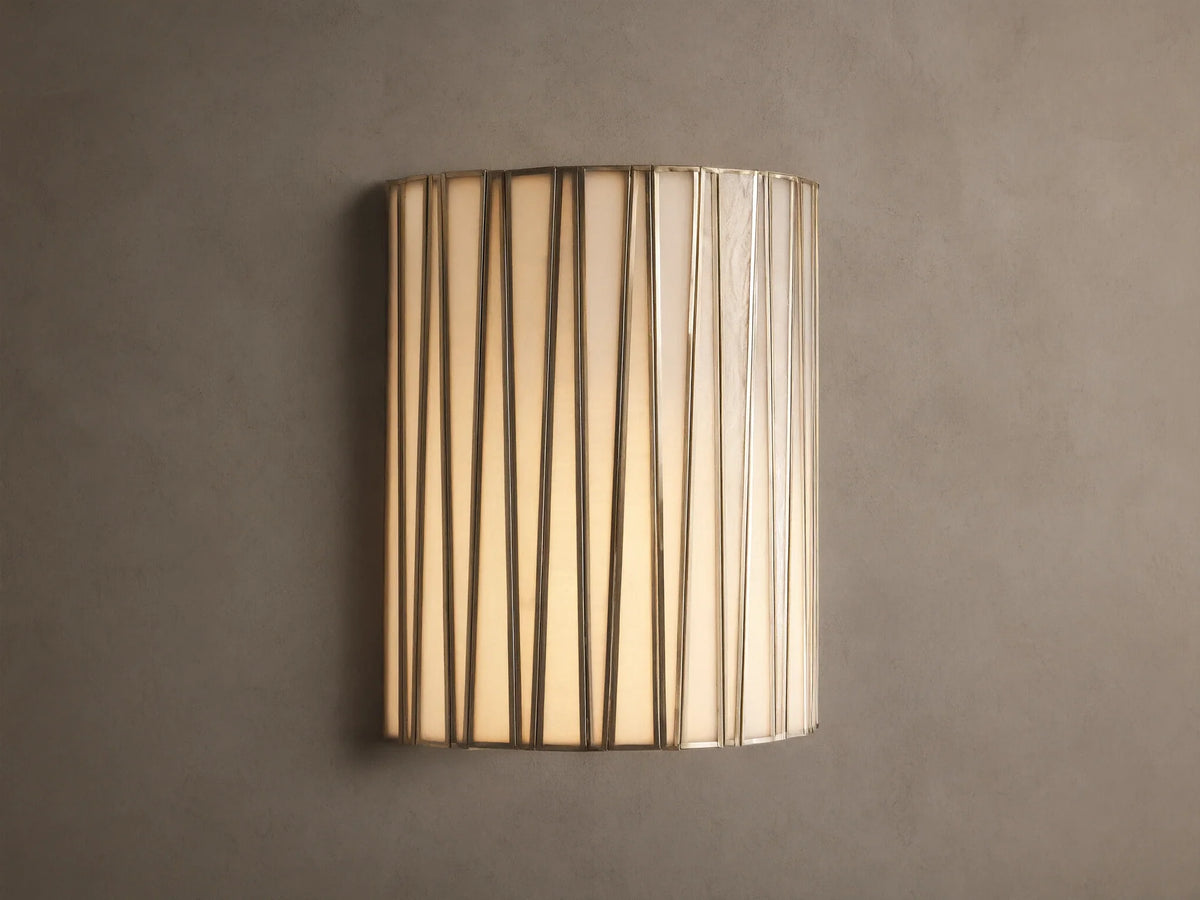 Jeunet Sconce, glowing, with vertical antiqued brass iron strips over translucent white glass, mounted on a neutral wall.
