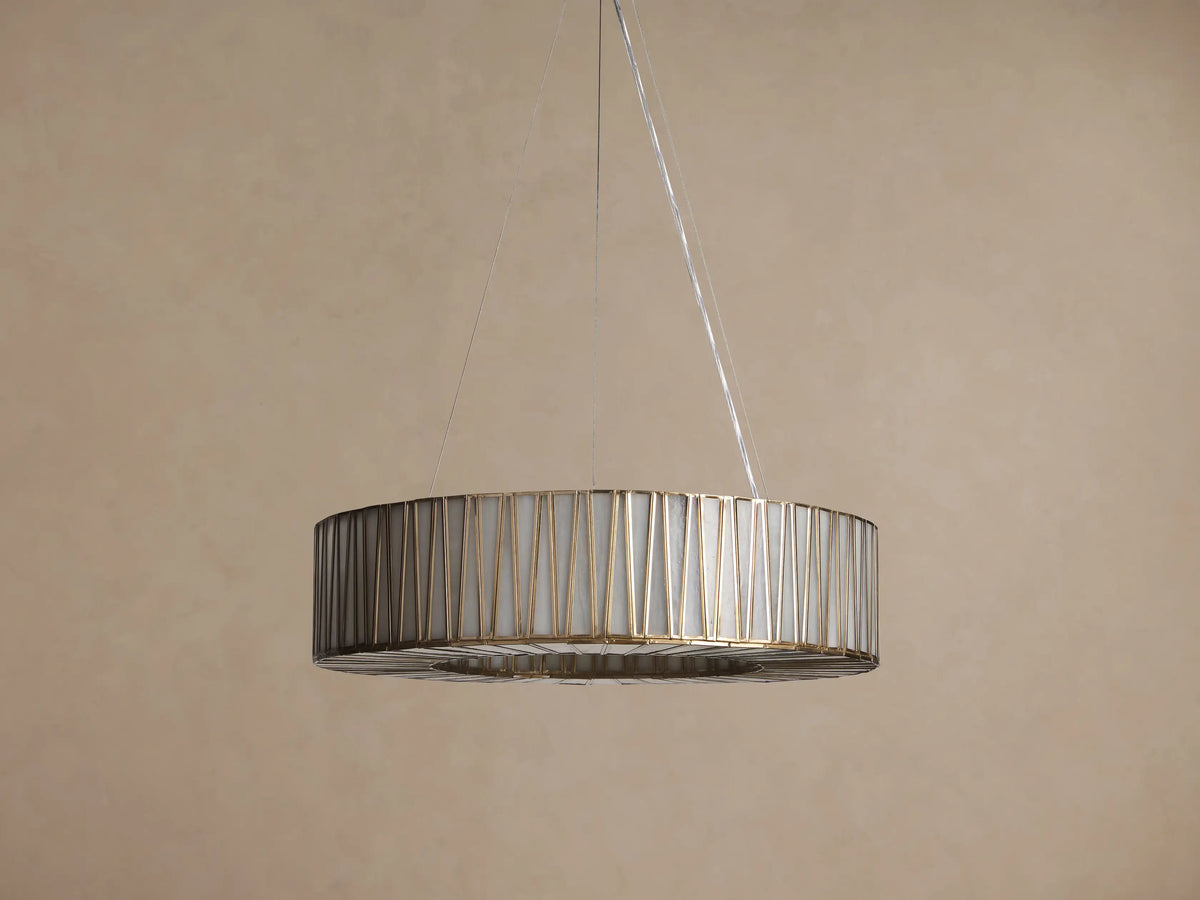 Jeunet Round Chandelier with antiqued brass geometric frame, illuminated cream glass panels, hanging from cables on a warm wall.