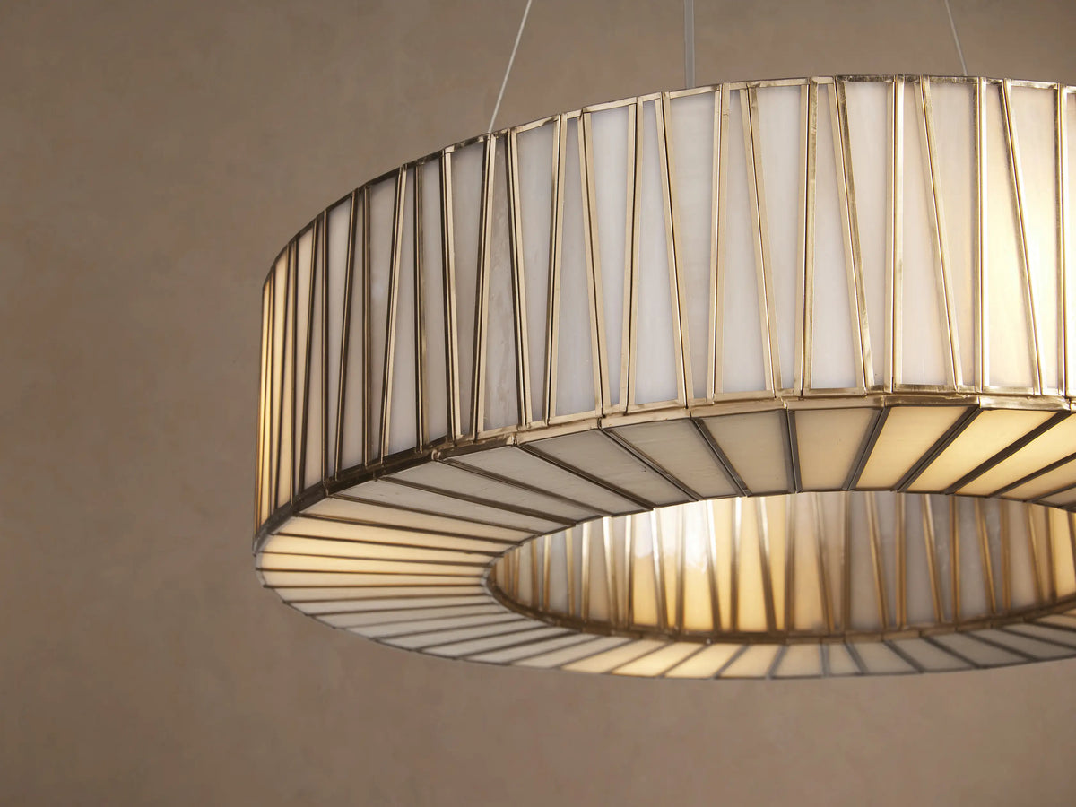 Jeunet Round Chandelier, antiqued brass frame with vertical glass panels, suspended against a light beige wall.