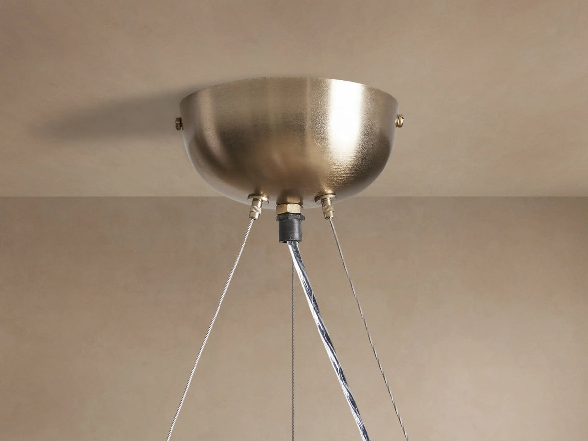 Close-up of a lit Jeunet Round Chandelier with an antiqued brass frame and geometric translucent glass panels, angled view.