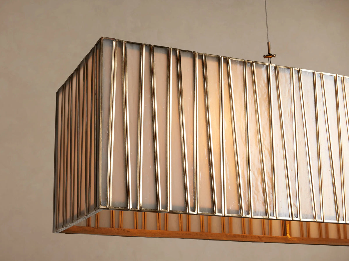 Jeunet Rectangular Chandelier with vertical antiqued brass bars over a light diffuser, suspended by cables on a beige wall.