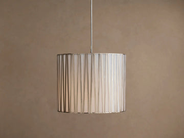 Hanging Jeunet Pendant light, cylindrical white shade with vertical antiqued nickel metal strips, softly glowing.