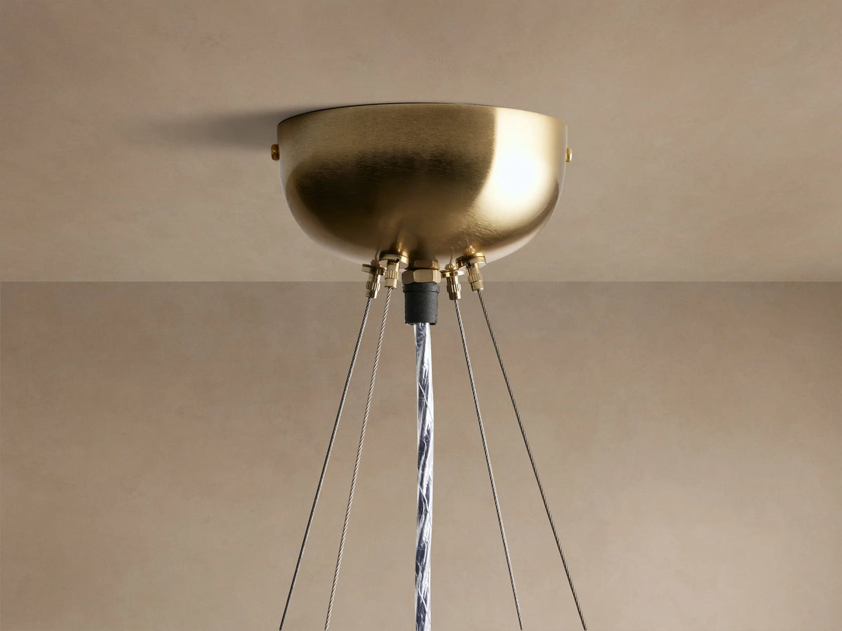 Close-up of a round Jeunet chandelier with vertical frosted glass panels and antiqued brass frames, glowing warmly.