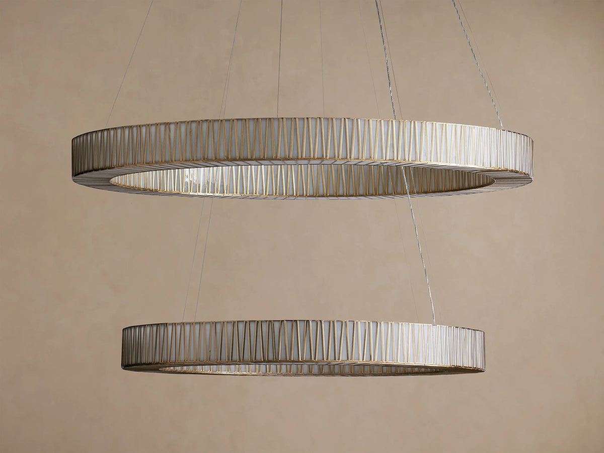 Jeunet 2-Tier Round Chandelier: Two illuminated, antiqued brass rings with vertical glass slats hang horizontally, glowing warmly.