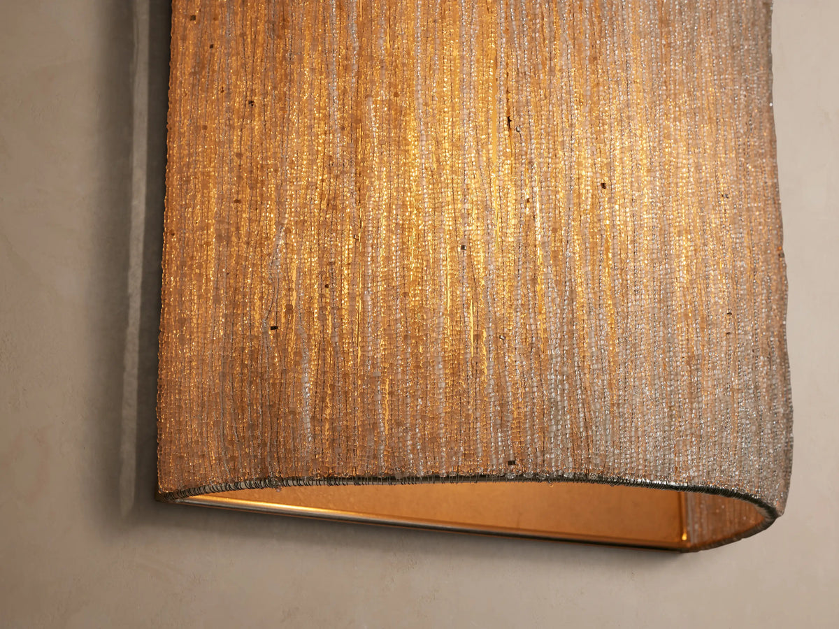 Vertical Romilly Beaded Sconce covered in individually strung light silver-toned glass beads, creating fine vertical strands, on a light brown wall.