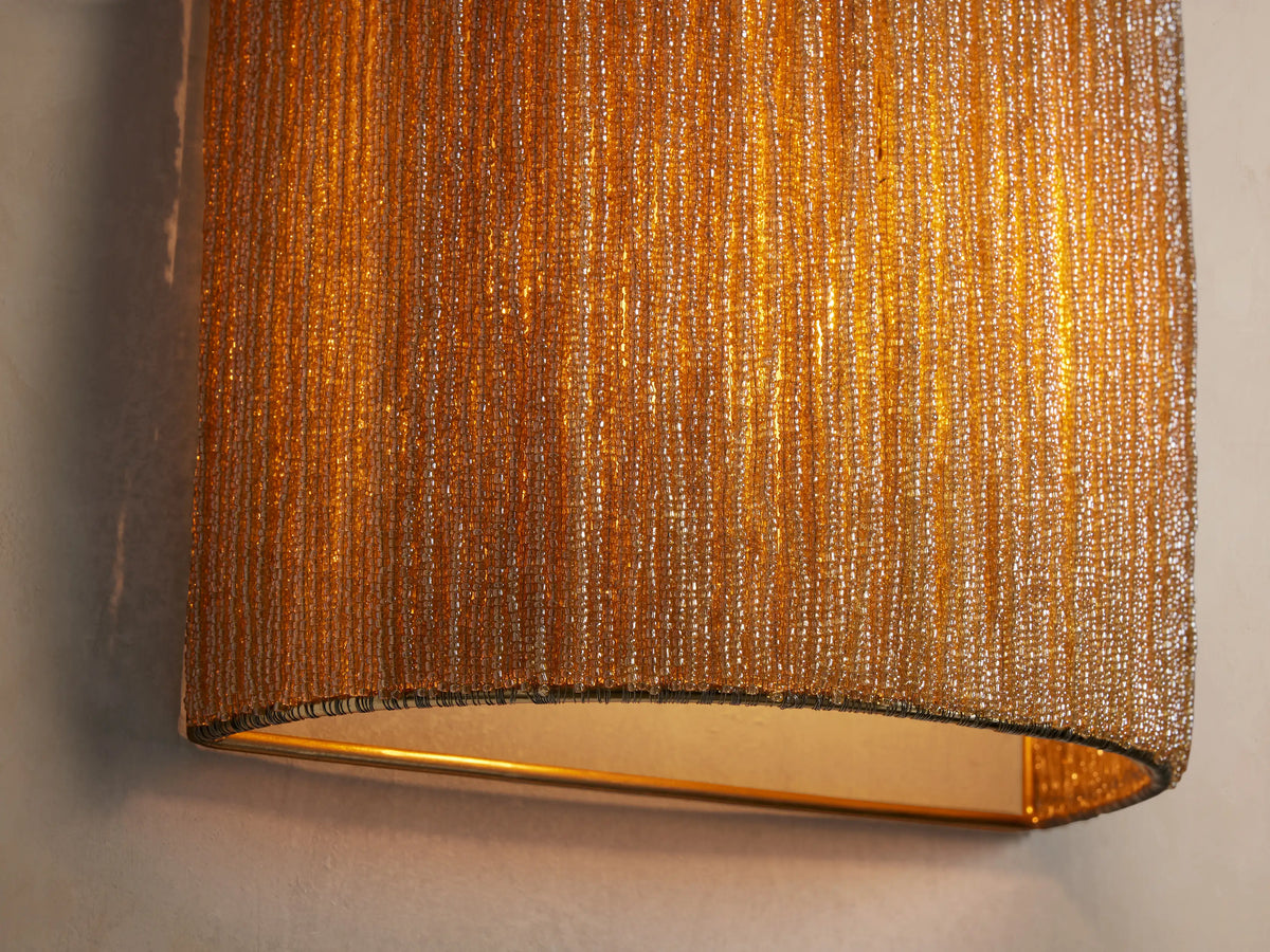 Romilly Beaded Sconce, vertical and curved, covered in dense, shimmering golden-bronze glass beads, mounted on a light wall.