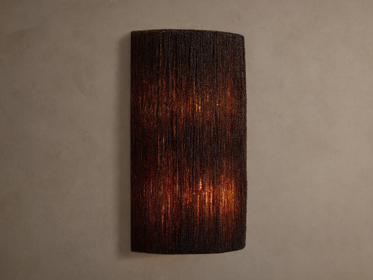 Romilly Beaded Sconce: Dark, rectangular fixture of individually strung glass beads, glowing warmly from within on a light wall.