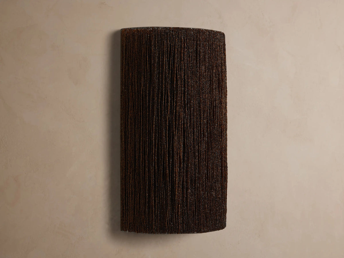Romilly Beaded Sconce: Dark, rectangular fixture of individually strung glass beads, glowing warmly from within on a light wall.