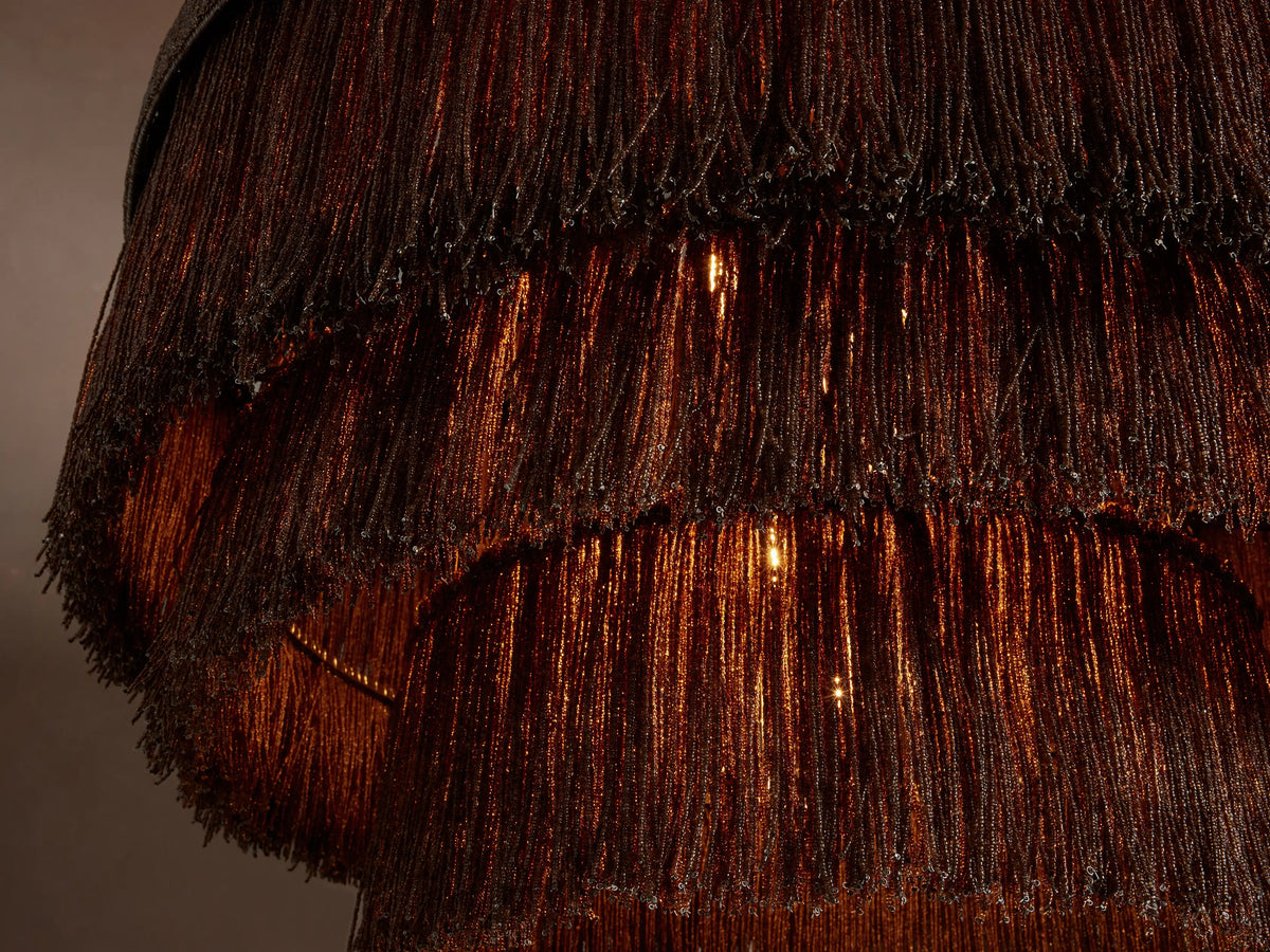 Romilly Tiered Chandelier. Dark brown, three-tiered design with fringed strands of glass beads, hanging against a plain wall.