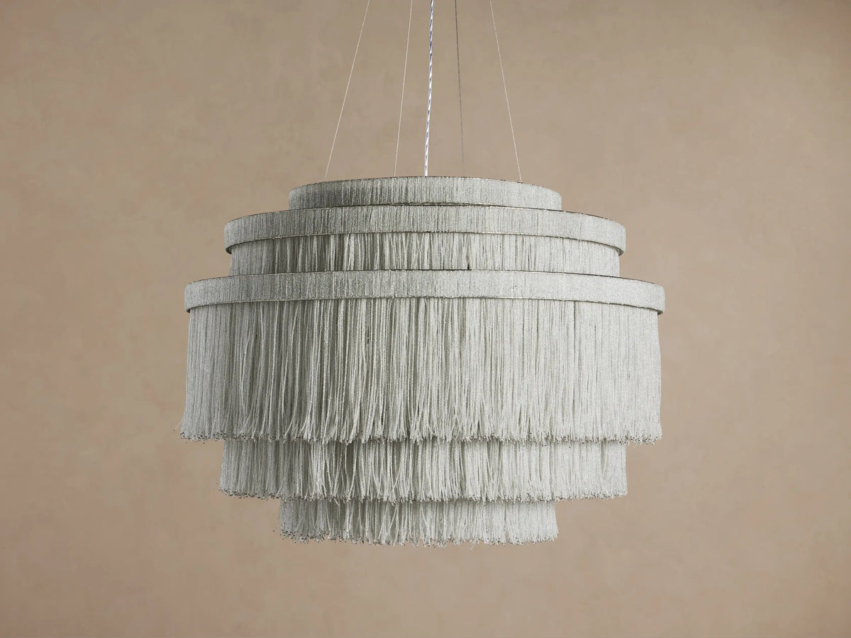 Romilly Tiered Chandelier, 4-tier circular design, light gray glass bead fringe glowing brightly, hanging against a neutral wall.