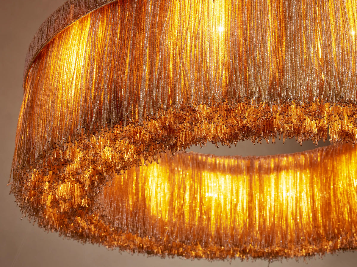 Romilly Round Chandelier glowing warmly, showing tiered concentric rings of shimmering golden glass beaded strands.