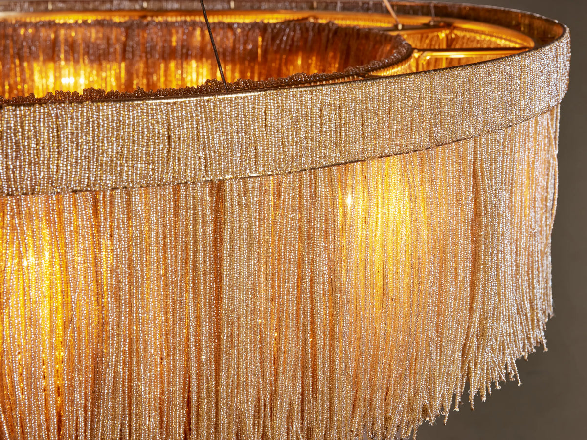 Close-up of Romilly Round Chandelier with golden glass beads forming a fringed shade, glowing warmly from within.