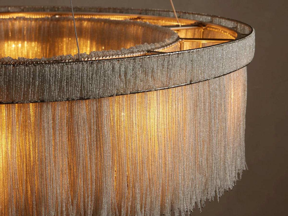 Close-up of Romilly Round Chandelier. Warm light glows through delicate strands of light glass beads on its circular, metallic frame.