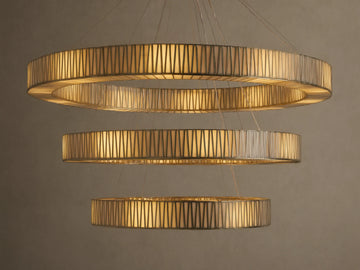 Jeunet 3-Tier Round Chandelier, illuminated with warm golden light, featuring three cascading rings of antiqued brass and textured glass.