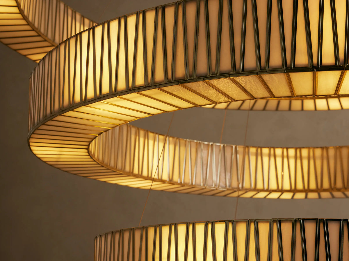 Jeunet 3-Tier Round Chandelier: 3 antiqued brass rings, each with geometric glass panels, hanging vertically against a light wall.