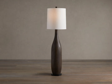 A tall Briar Floor Lamp with a dark espresso, slender wooden base and a glowing white linen cylinder shade on a wooden floor.