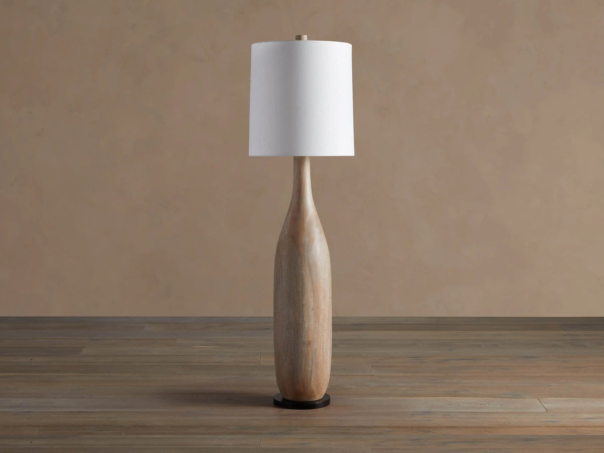 Briar Floor Lamp: natural wood, bottle-shaped base, with a white cylindrical linen shade, standing upright on a wood floor.