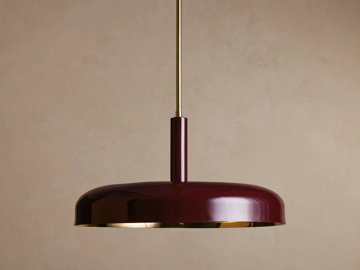 A burgundy ceiling pendant light with a glossy finish, round shape, and brass rod, set against a neutral brown background.