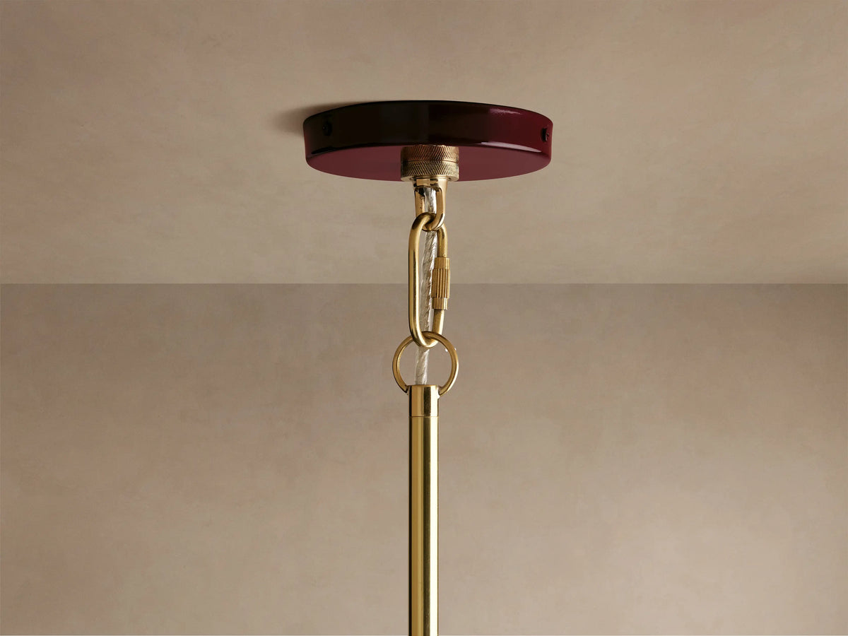 Close-up of a glossy maroon pendant light with a shiny golden interior, featuring a glowing bulb inside.