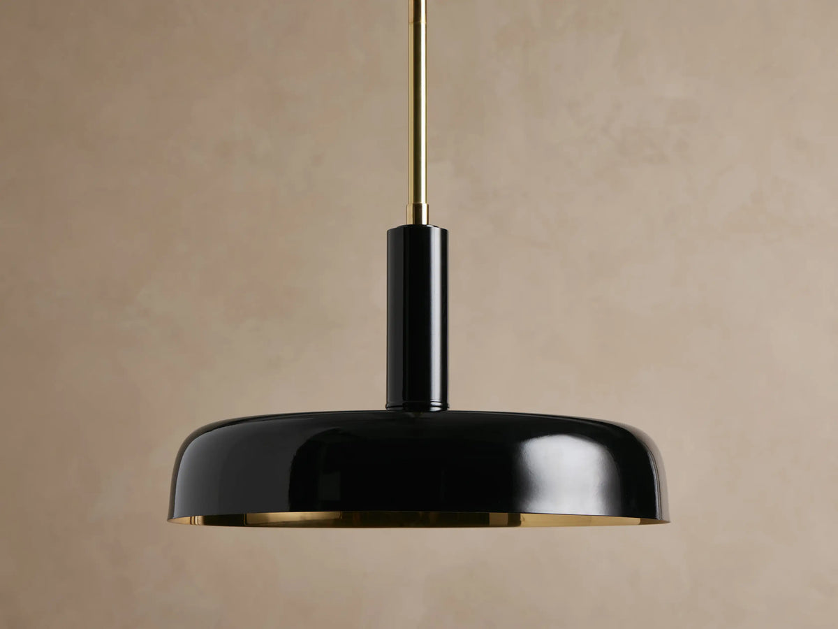 Bonham Pendant: sleek black metal domed shade with a gleaming brass interior, suspended from a brass rod against a textured beige wall.