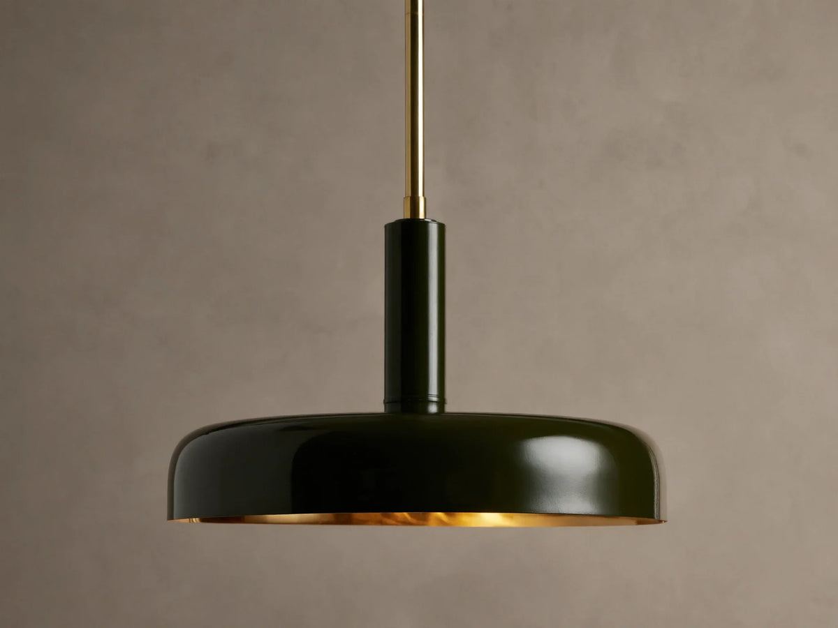 Bonham Pendant: Dark green dome-shaped light with a brass interior hangs from a brass rod against a textured warm grey wall.