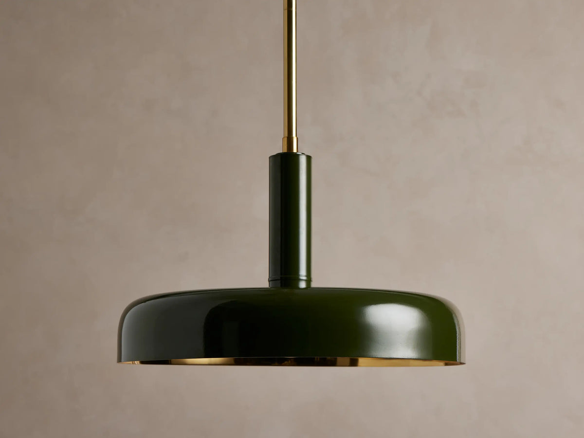 Bonham Pendant: Dark green dome-shaped light with a brass interior hangs from a brass rod against a textured warm grey wall.