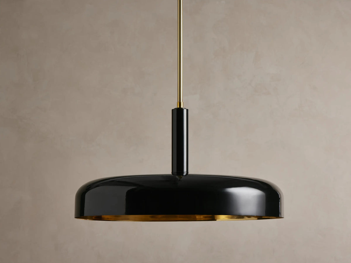 Bonham Pendant: a sleek black dome-shaped light with a reflective brass interior, hanging from a thin brass rod against a wall.