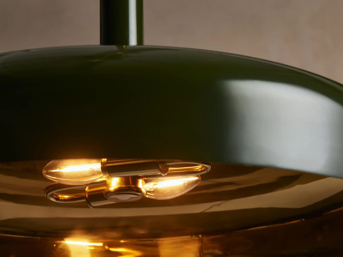 Bonham Pendant: Dark green, wide dome light with shiny brass interior, suspended from a brass rod against a beige wall.