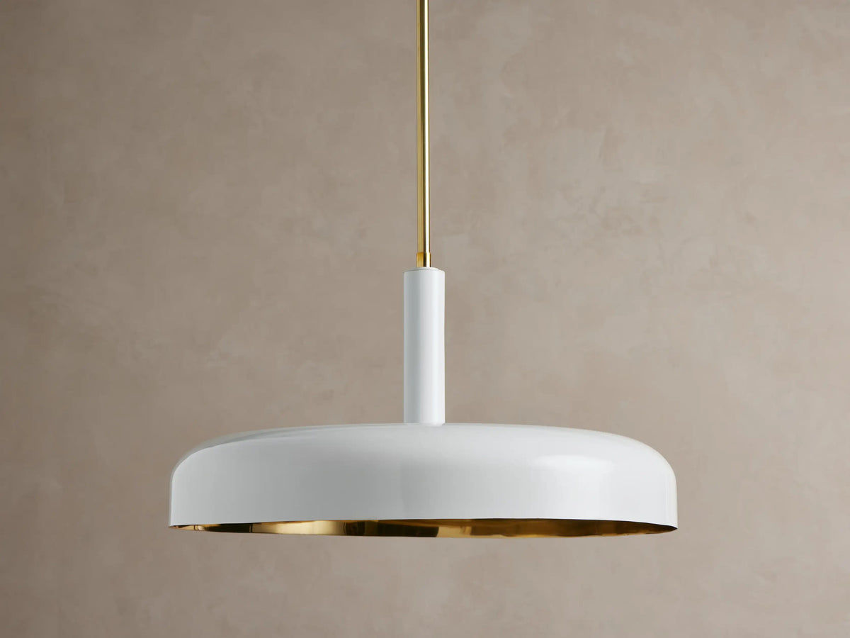Bonham Pendant: Light grey powder-coated lamp with warm brass interior, glowing and suspended from a slender brass rod.