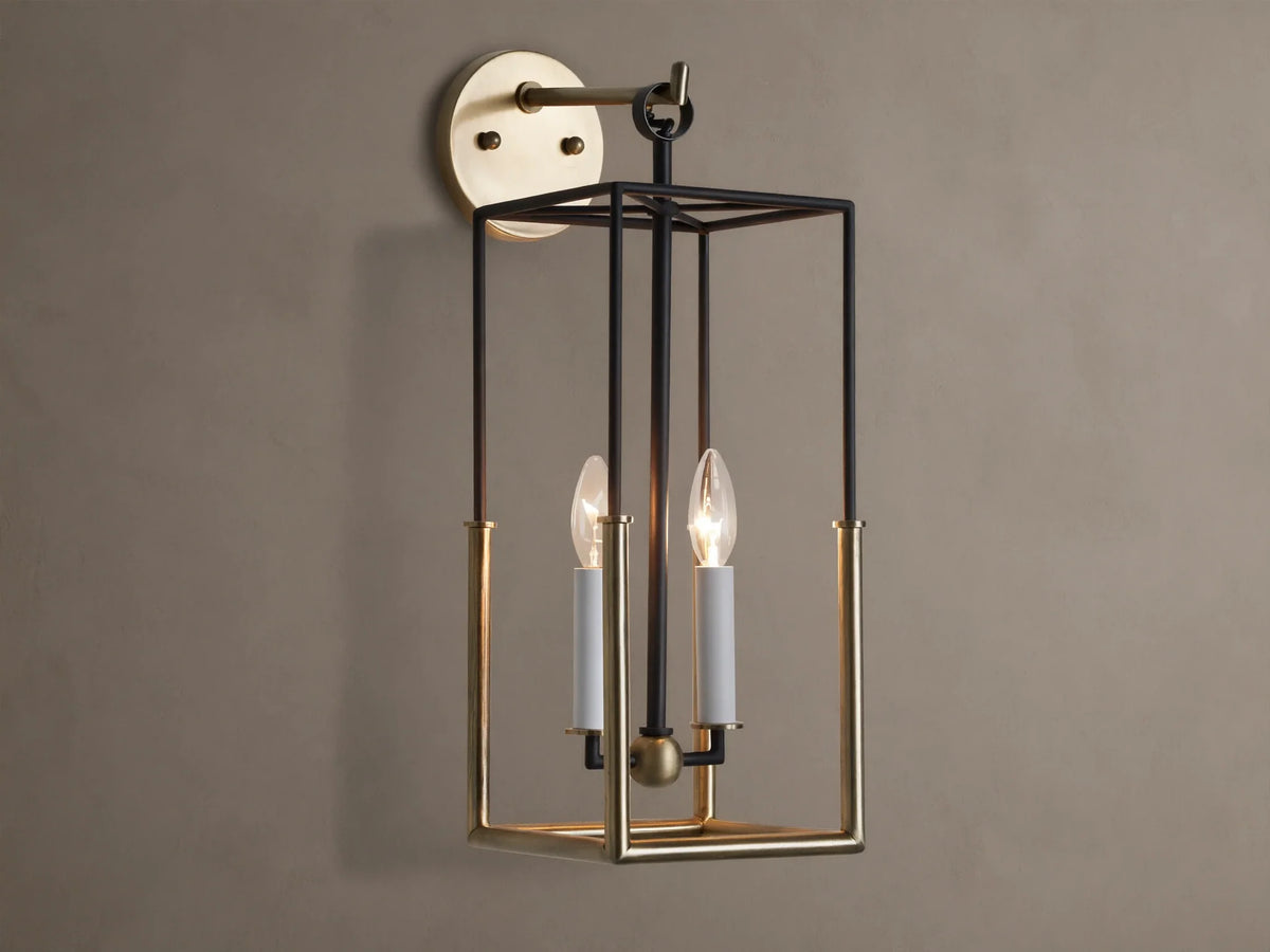 Holt Sconce: rectangular lantern-style light with black iron and antiqued brass frame, two lit candle-style bulbs on neutral wall.