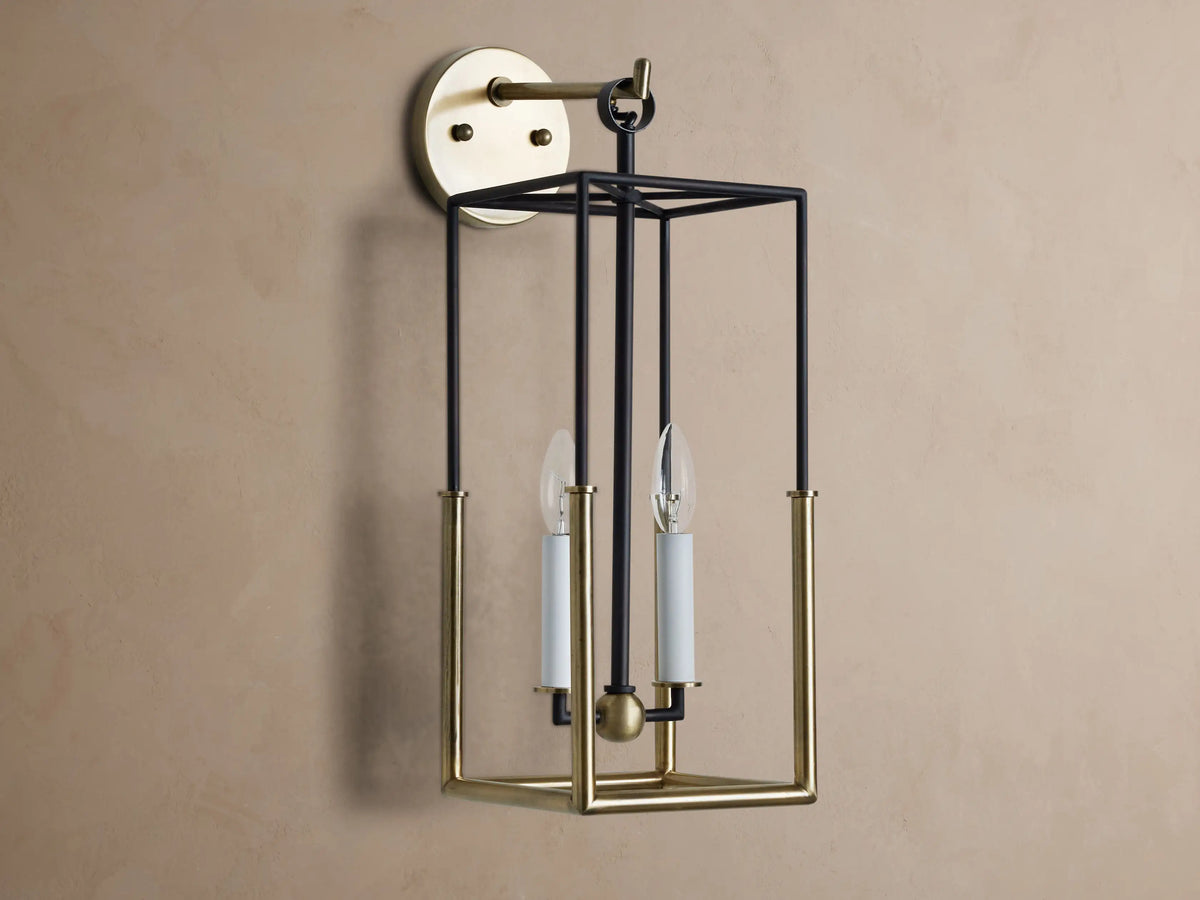 Holt Sconce: rectangular lantern-style light with black iron and antiqued brass frame, two lit candle-style bulbs on neutral wall.