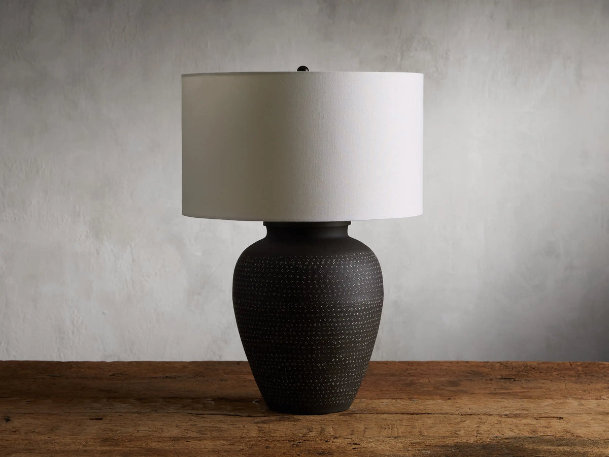 Two Howell Table Lamps with embossed powder-coated bases and white cotton linen shades, one larger and one smaller, on a wooden surface.