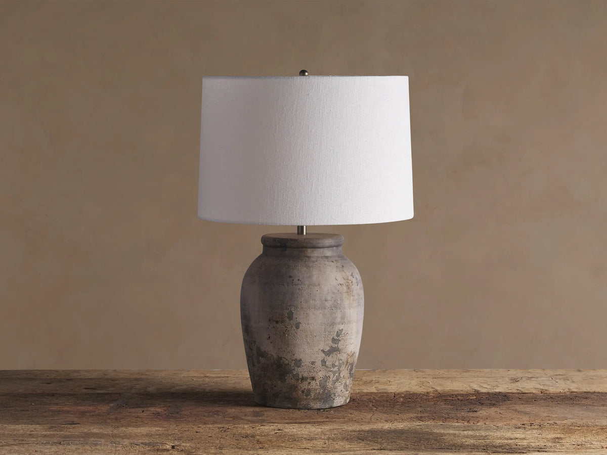 Thornton Table Lamp with distressed dark grey terracotta base, light linen drum shade, on a rustic wooden table.
