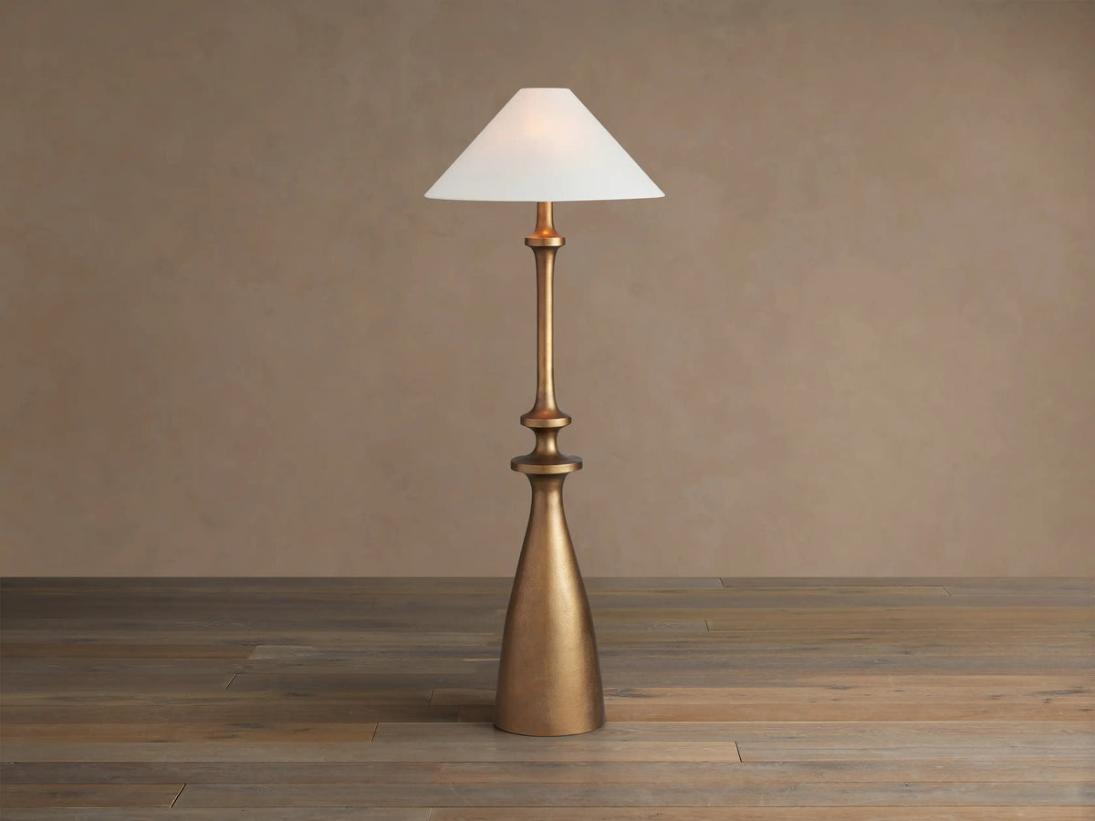 Murphy Floor Lamp with a brass-finished cast aluminum base and stem, topped with a white conical linen shade, standing on wood floor.