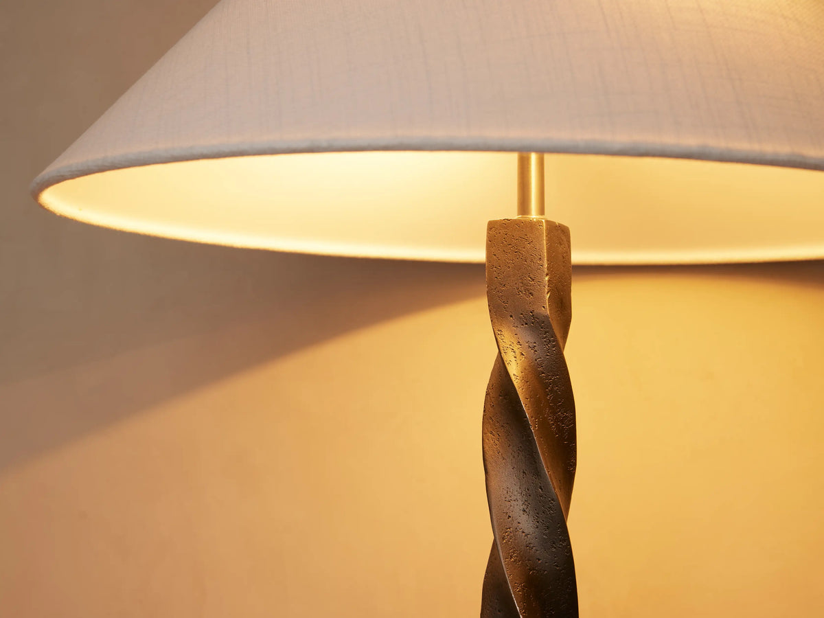 A twisted metal table lamp with a conical white shade on a wooden surface against a neutral wall background.