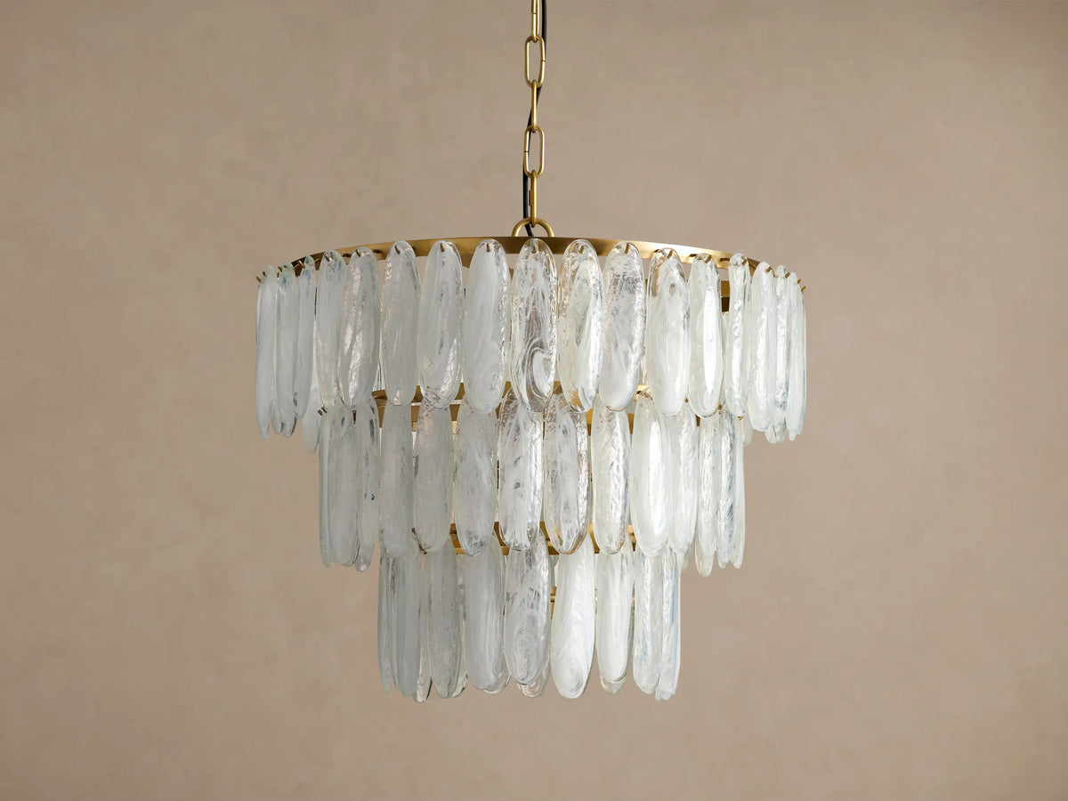 Verna Chandelier. Multi-tiered, antique brass frame with numerous textured, translucent swirled glass pieces, softly glowing.