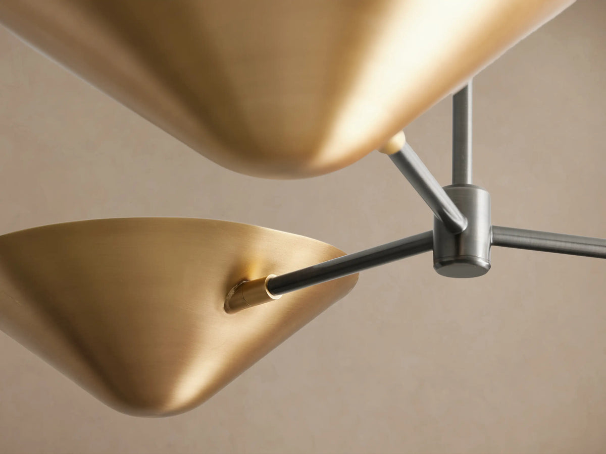 Simms Flush Mount: A modern ceiling light with three conical antique brass shades on dark bronze arms, one shade lit.