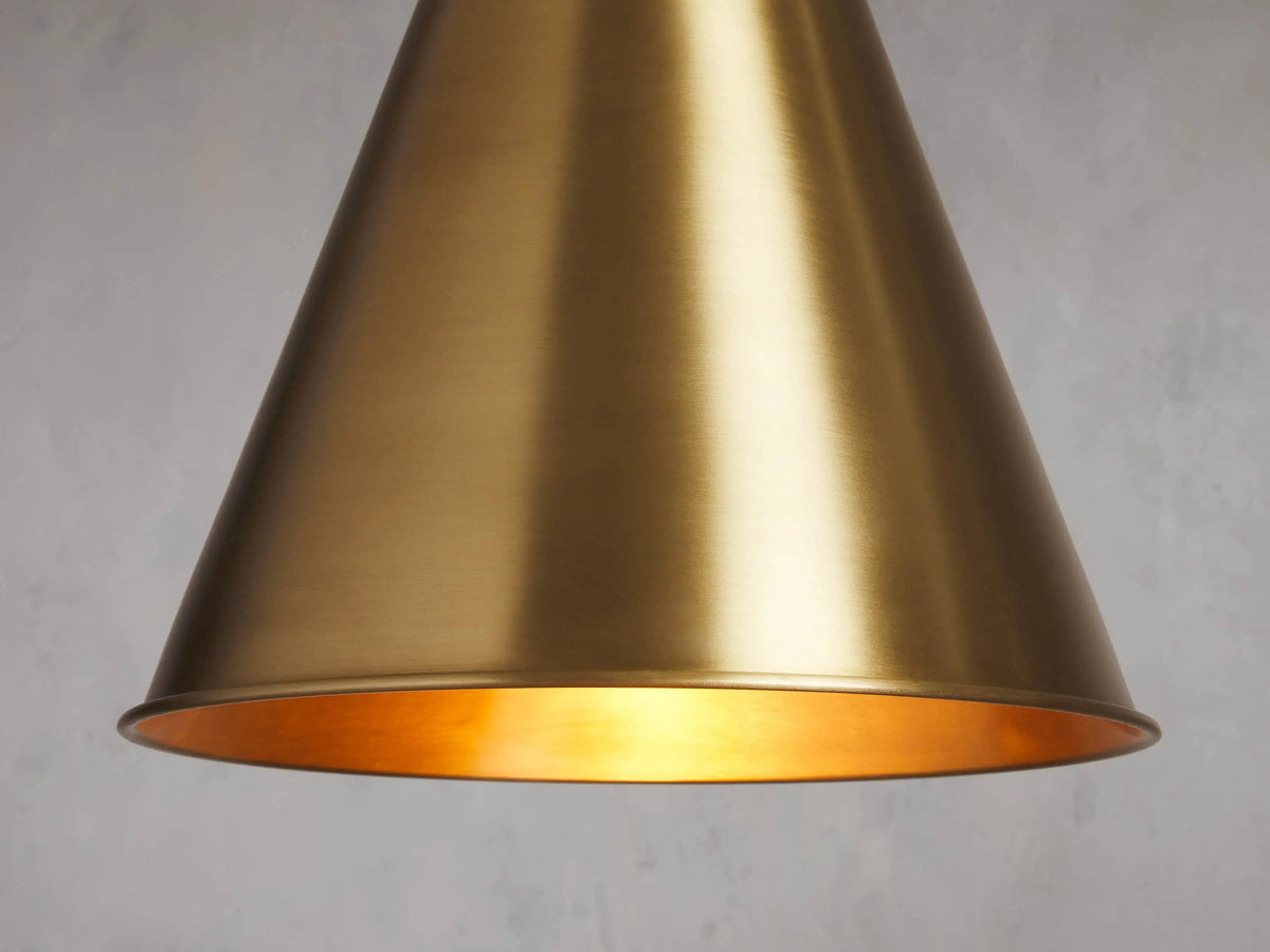 Cone-shaped Watley Pendant in polished brass with an oxidized antique brass interior. Smooth metallic finish, warm glow from within.